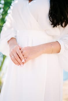 Bride folded her hands in front of her standing by the sea. Cropped. Faceless. High quality photo