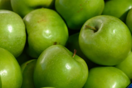 Bright green apples lay piled high, showcasing their glossy skin under the warm sunlight. Their crisp texture and sweet aroma invite shoppers to explore the market's bounty.