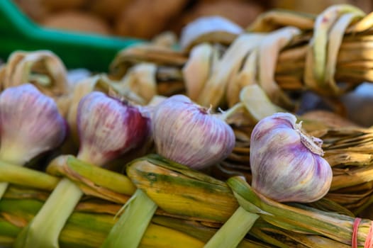 Freshly harvested garlic showcases its purple hues, carefully arranged in a handwoven basket amidst the bustling ambiance of a local farmers market in late summer.