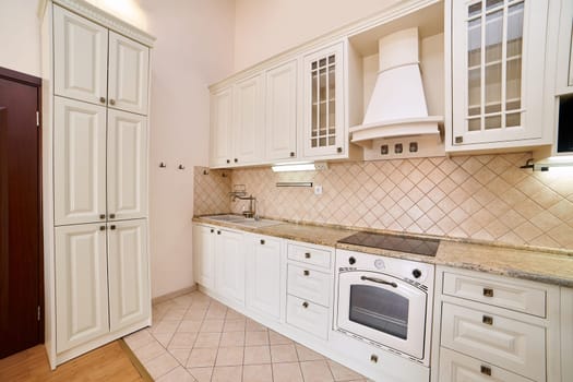 Beige kitchen with white cabinets, stove, hood and large closet. High quality photo