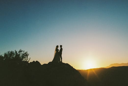 Bride and groom stand on the mountain holding hands at sunset. High quality photo