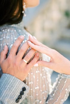 Bride put her hand on the hand of groom hugging her shoulder. Back view. Cropped. High quality photo