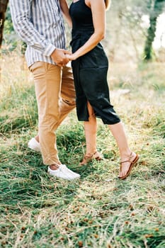 Man and woman stand holding hands in a green grove. Cropped. Faceless. High quality photo