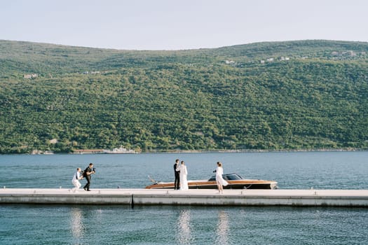 Photographers take pictures of bride and groom standing on the pier near a motor boat. High quality photo