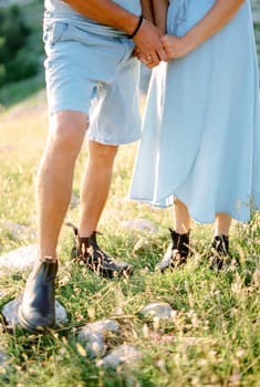 Husband and wife stand holding hands on a sunny lawn. Cropped. Faceless. High quality photo