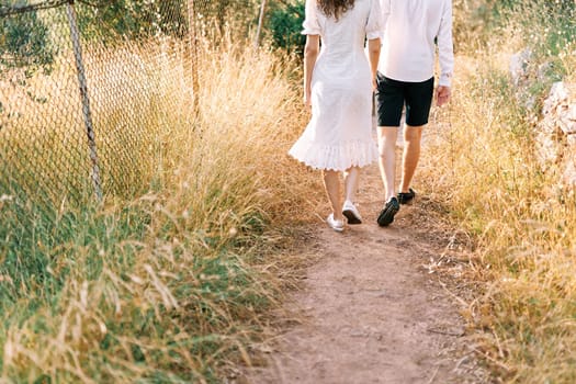 Couple walk along a country road in a field. Back view. Cropped. High quality photo