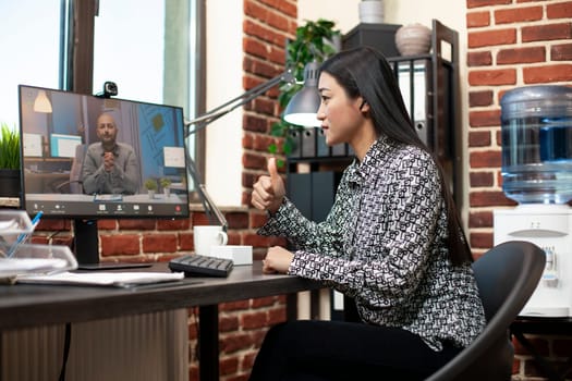 Businesswoman and male client collaborate on project updates during an online meeting. Female manager giving thumbs up to colleague and discussing business development plans in videoconference.
