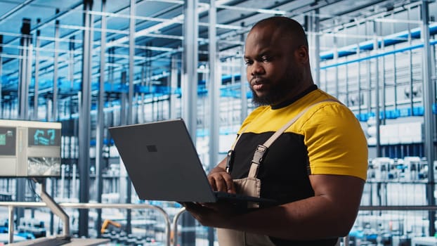Smart factory professional implements automated workflows and control systems using laptop, computerizing manual operations. Man integrates sensors into production using notebook, camera A