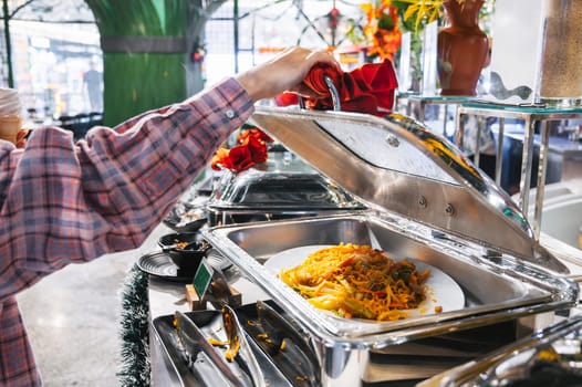 hot dishes in pots on buffet table at the self-service restaurant in the hotel. A woman's hand opens a tray of food