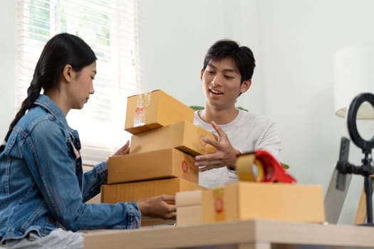 An entrepreneurial couple collaborates in their living room, packing boxes and preparing their shipment deliveries, displaying teamwork and dedication to their business.