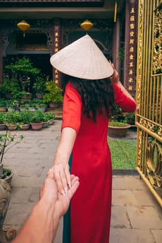couple's trip to Asia in Vietnam. Follow me with the back of a female traveler tourist in a Vietnamese hat at a temple in Vietnam in Asia