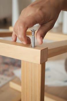 A hand is securing a screw into a wooden table leg during assembly.