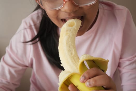 A child bites into a ripe banana while sitting indoors.