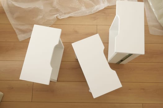Three white furniture pieces are placed on a light wooden floor indoors.