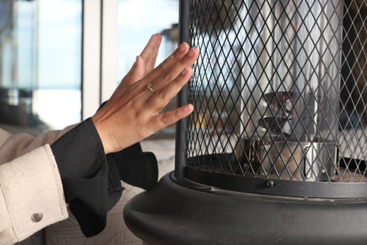 A hand reaches towards a heater for warmth in a cozy indoor setting.