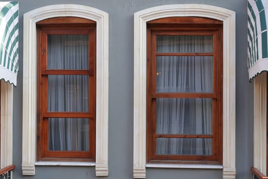 Two wooden windows with sheer white curtains framed in a gray wall.
