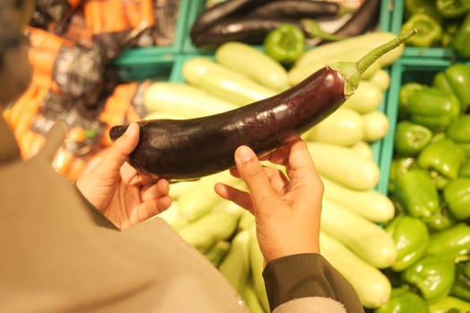 A person inspects a purple eggplant among various fresh produce.