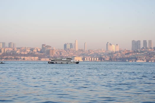 Ferry travels across the water with a city skyline glowing at dusk.