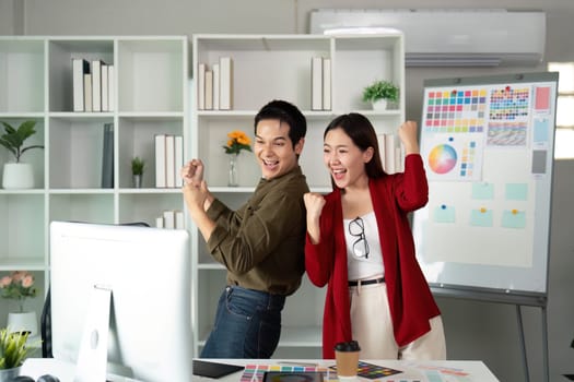 With excitement, the two designers express their happiness over a successful project outcome, showcasing teamwork in a lively office environment.