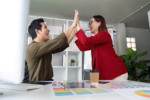 In a creative atmosphere, two designers express joy by high-fiving each other, emphasizing teamwork and accomplishment in their project.