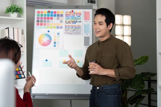 During a brainstorming session, a male designer enthusiastically gestures to his colorful presentation, engaging a seated colleague in meaningful design discussions.