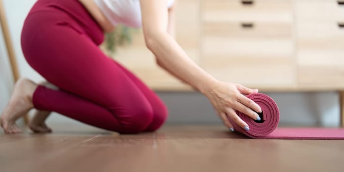 A woman concludes her yoga practice by rolling up her mat, symbolizing the end of a mindful and introspective session.
