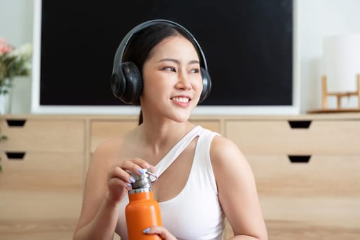 Focusing on wellness, a woman admires her orange water bottle, preparing to stay hydrated during her fitness regime.