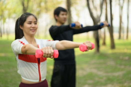 Young couple exercising with dumbbells in a peaceful park. Wellness and healthy lifestyle concept.