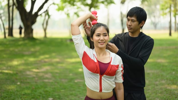 Young couple exercising with dumbbells in a peaceful park. Wellness and healthy lifestyle concept.