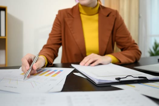Close up of businesswoman analyzing financial charts and reports at a modern office desk.