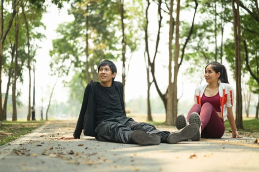 Young couple sitting on the ground of a park path and enjoying a calm moment after exercising.