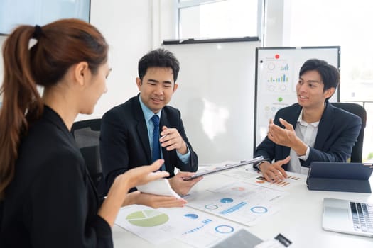 A diverse business team engages in a strategic meeting, analyzing charts and graphs to enhance their project outcomes. Their body language reflects active discussions and collaboration.