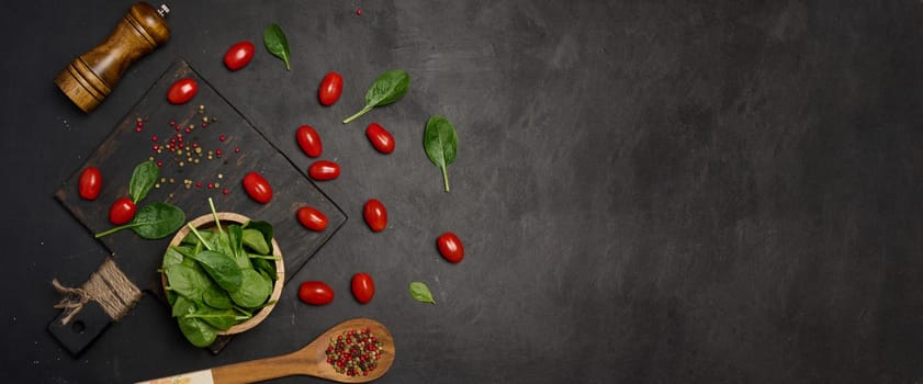 Fresh spinach leaves, cherry tomatoes, and mixed peppercorns on a black background. Copy space