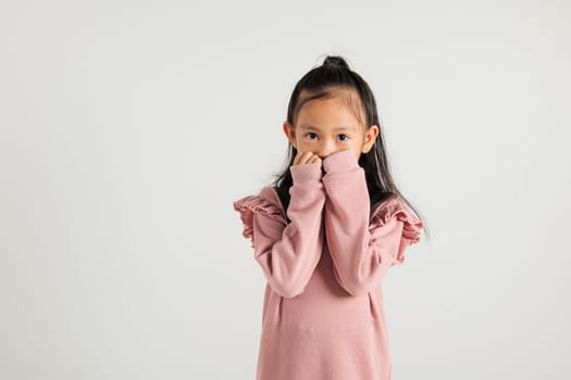 Asian portrait cute young kid girl standing amazed, shocked afraid mouth covered gesturing hand palms looking camera, studio shot isolated on white background, Thai kindergarten child scared