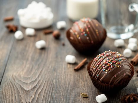 Chocolate cocoa bomb on wooden table near cup and plant-based milk. Ball made from milk chocolate with marshmallow, copy space for text. Trendy winter drink, gift present idea for christmas holidays