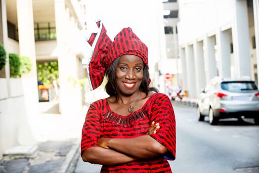 mature african woman standing outdoors head tied with a piece of loincloth watching the camera smiling.