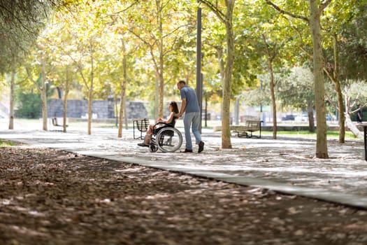 Nurse assisting a female patient in a wheelchair through a sunny park, providing mobility support and enjoying the outdoors