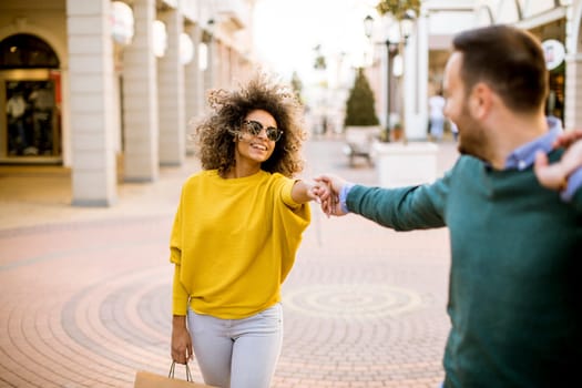 Young and cheerfull couple walking along street with shopping bags