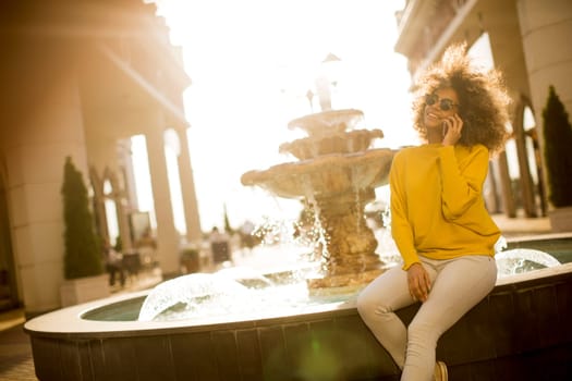 Attractive young woman with curly hair using her touch screen mobile cell phone by the fountain