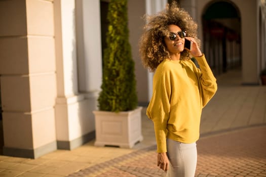 Attractive young woman with curly hair using her touch screen mobile cell phone on the street