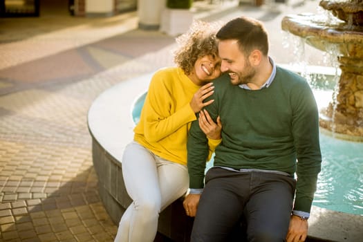 Portrait of beautiful smiling love couple sitting near fountain outdoors
