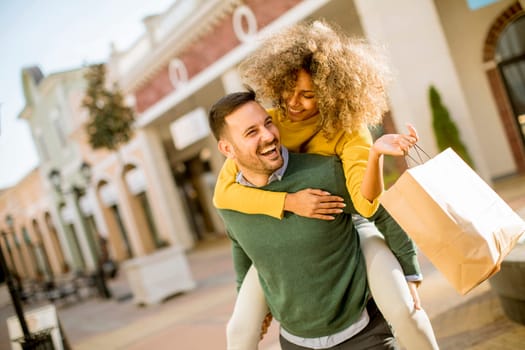 Portrait of  young man holds young woman on his back , have fun and go to shopping