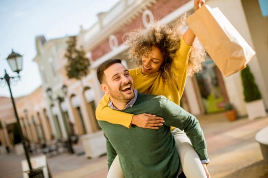 Portrait of  young man holds young woman on his back , have fun and go to shopping