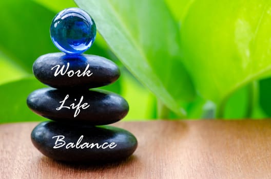 Work Life Balance text on black zen stones with blue glass marble on top. Life balance concept.
