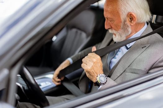 Sophisticated senior man in a suit fastening his seatbelt, ready for a journey