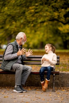 Handsome grandfather playing red hands slapping game with his granddaughter in park on autumn day