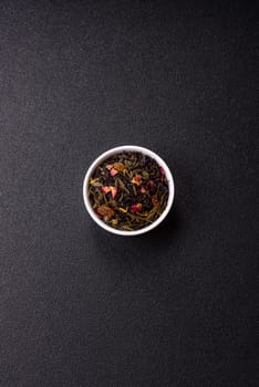 Dry tea mix blend black, green and flower petals in bowl on dark concrete background