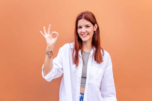 young woman doing ok sign with hand while smiling looking at camera in a positive and friendly mood suggesting that she is happy and content, copyspace for text