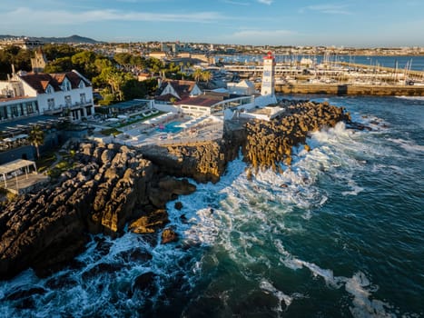 Aerial view of Santa Marta lighthouse and Cascais marina with moored yacht boats with Cascais cityscape, Portugal on sunset