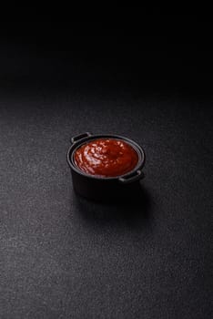 Red sauce or ketchup with salt and spices in ceramic sauce boat on dark concrete background